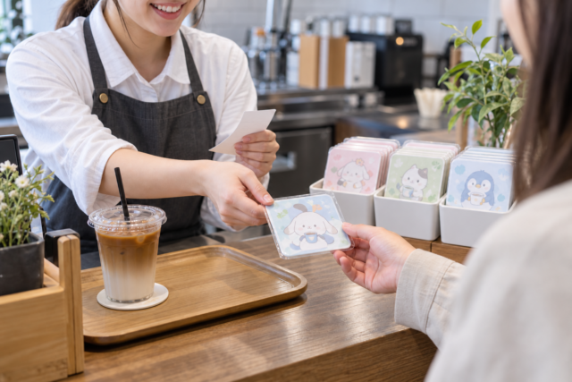 注文内容を確認して特典コースターを渡すカフェスタッフの手元