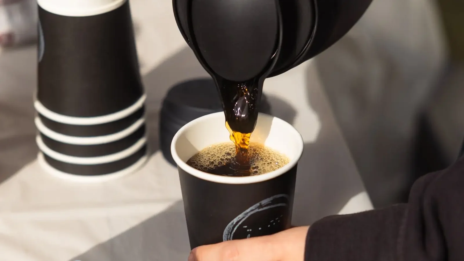 ポットからde.coffee roastersの紙カップへコーヒーを注ぐ公式写真