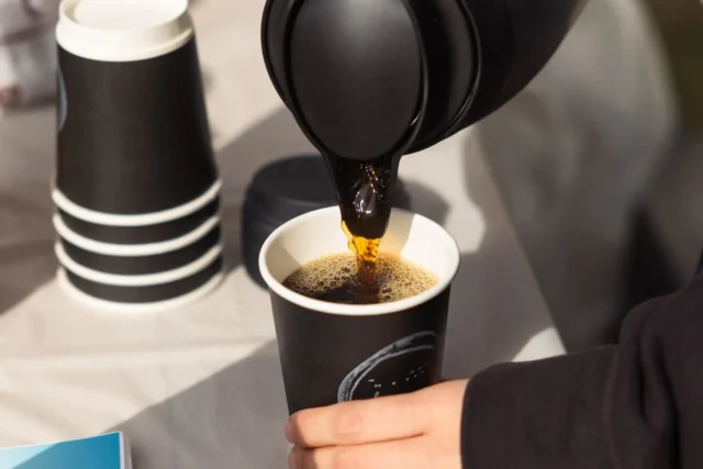 ポットからde.coffee roastersの紙カップへコーヒーを注ぐ公式写真