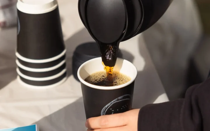 ポットからde.coffee roastersの紙カップへコーヒーを注ぐ公式写真