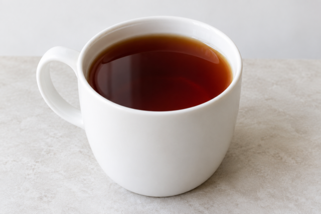 白いカップに入った濃い色の紅茶のイメージ