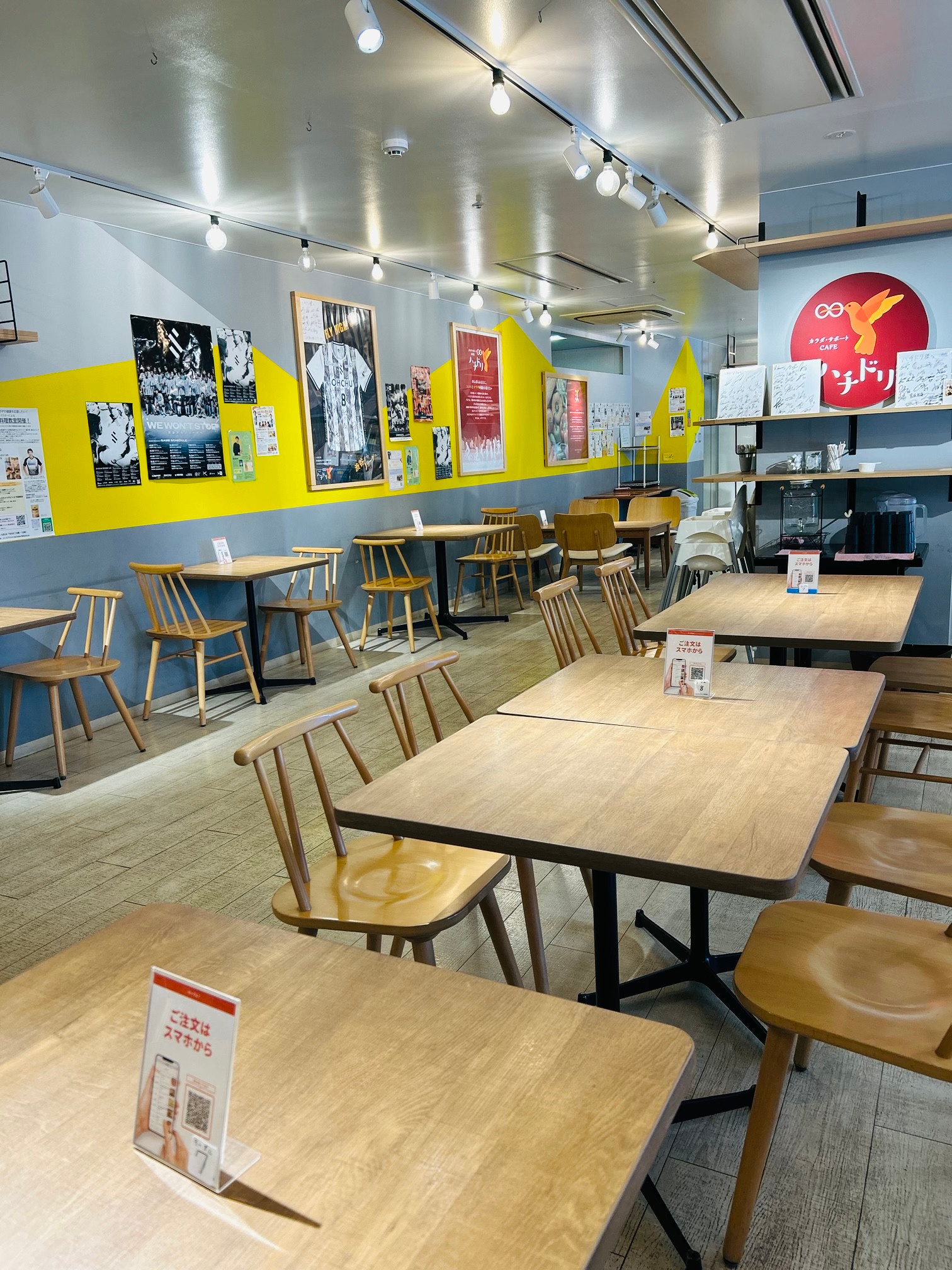 黄色とグレーの壁、木製のテーブルと椅子が並ぶハチドリの店内