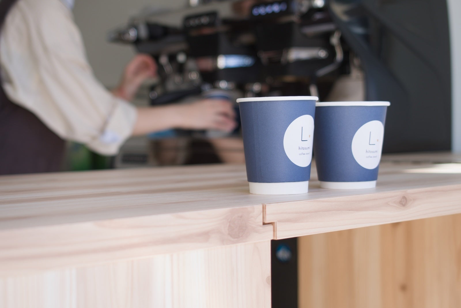 hitosumi coffee standの木製カウンターに並ぶ紙カップと奥のコーヒーマシン