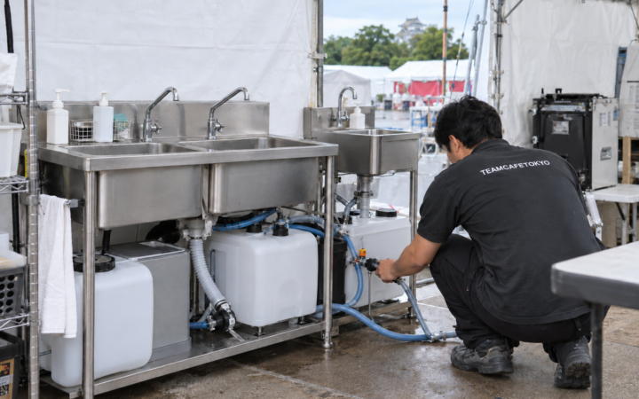 仮設厨房のシンク・給排水タンクと接続部を点検するスタッフ
